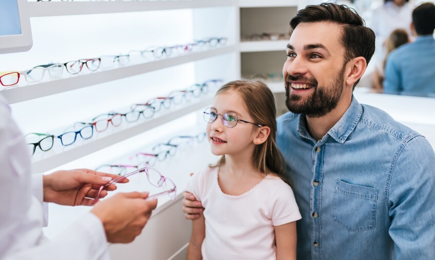 little girl and man picking out glasses with optometrist