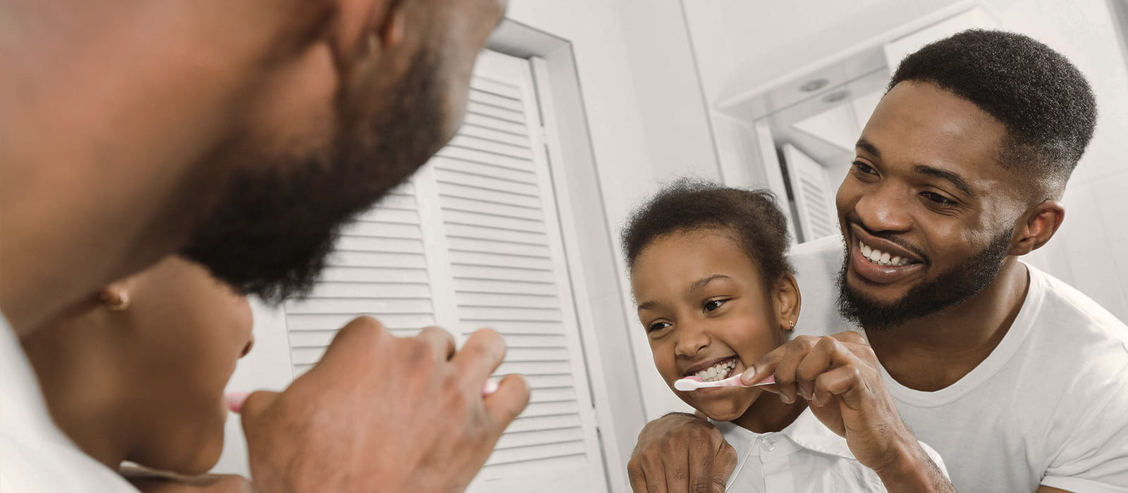 Father helping daughter brush her teeth.