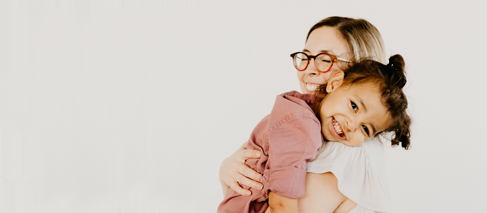 young girl smiling at the camera while being hugged by her mother