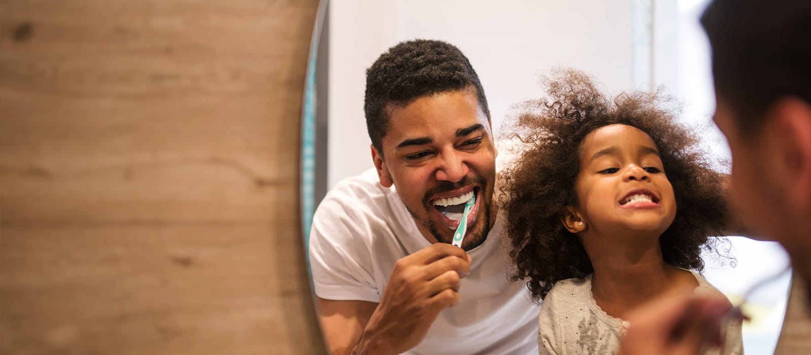 Father and daughter laughing while brushing their teeth together.