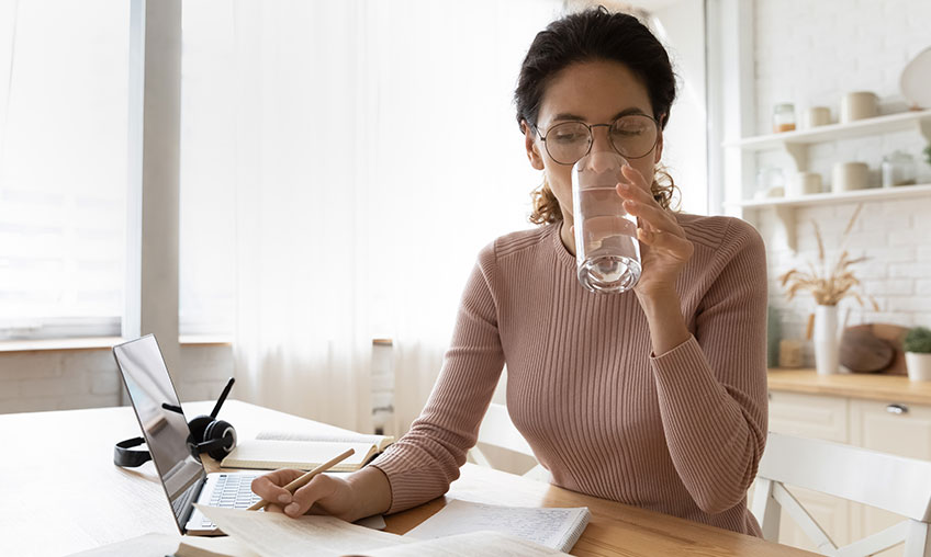 mujer bebiendo agua de un vaso mientras trabaja desde casa